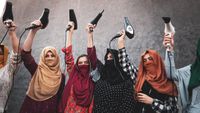 A row of Afghan refugee women in brightly coloured headscarves, most with their faces veiled, stand against a grey concrete wall holding hairdryers triumphantly above their heads, cables dangling. 
