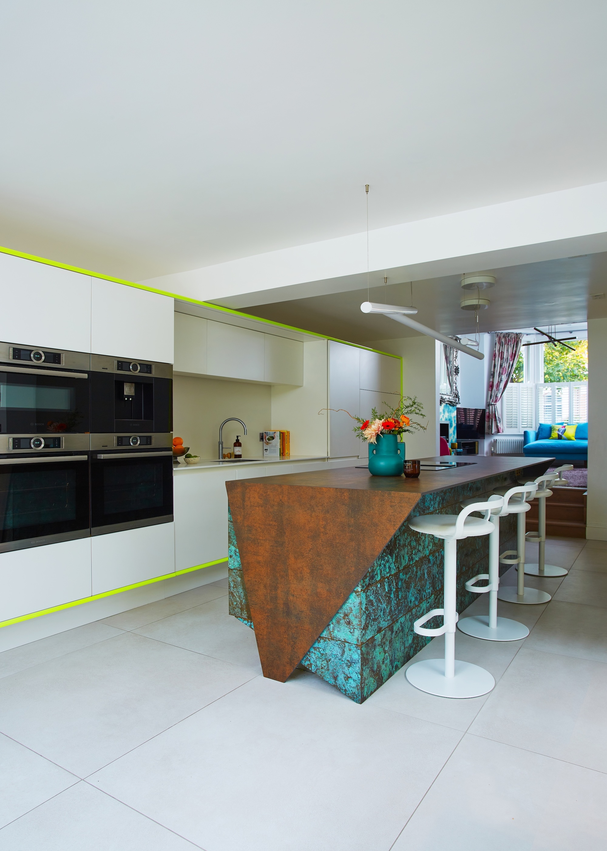 A modern kitchen with white slab cabinets, a geometric shaped island, and neon trim panels