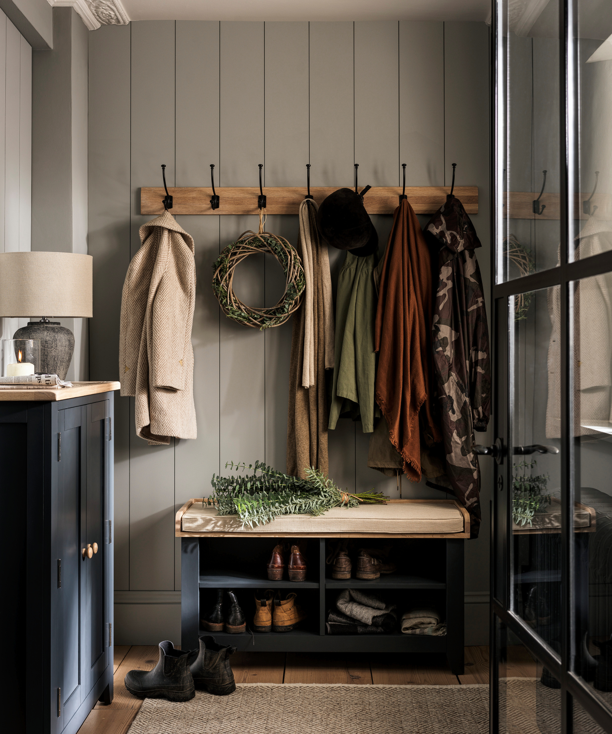 inside of small porch with wood panelled walls, hooks on walls, coats and shoe storage bench