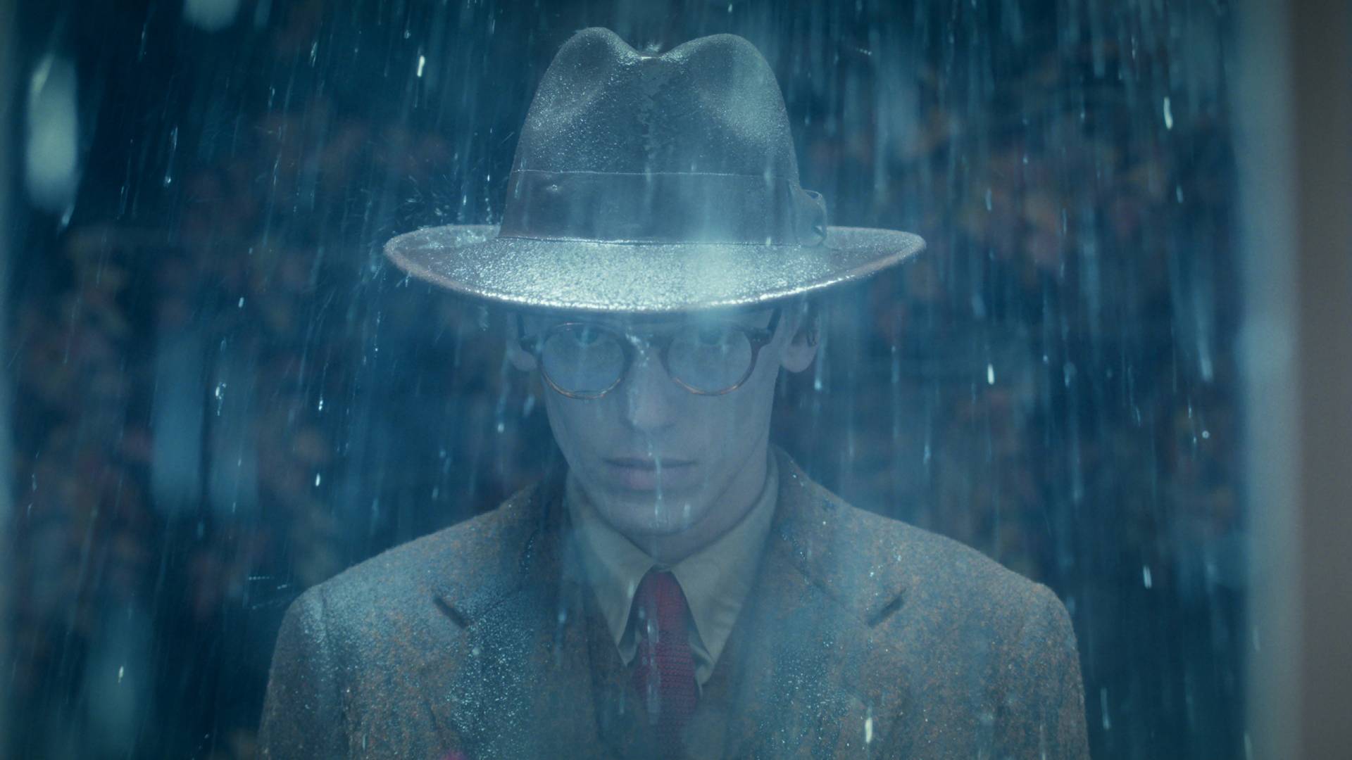 Jamie Campbell Bower as Mr. Whatsit in Stranger Things season 5 volume 2, standing in the rain wearing a rimmed hat