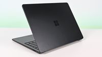 Surface Laptop for Business 8th Edition with a closed screen featuring a Windows logo, resting on a white surface. The background is a soft gradient from light blue to green.