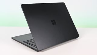 Surface Laptop for Business 8th Edition with a closed screen featuring a Windows logo, resting on a white surface. The background is a soft gradient from light blue to green.