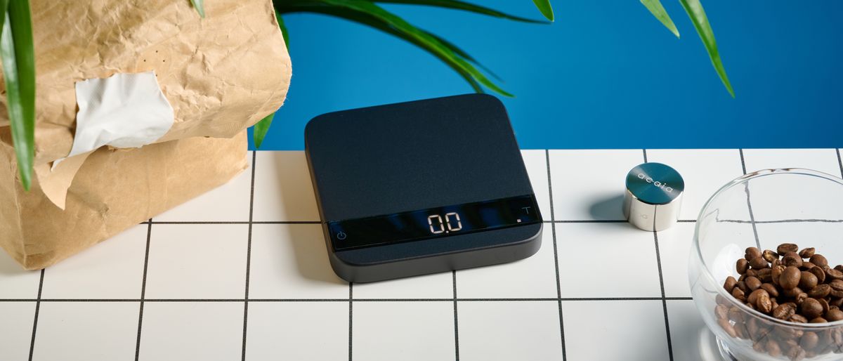 the acaia lunar coffee scale in black with an aluminum surface and accurate precise weight ideal for espresso machines given its compact size is photographed againt a blue tom&#039;s guide background