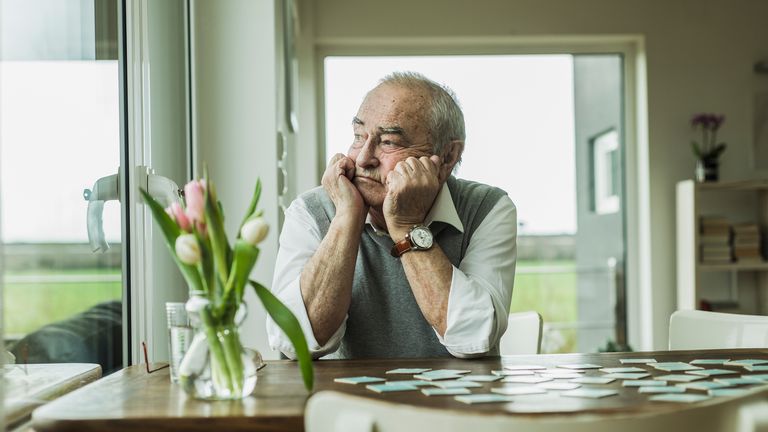 Older man sits at a table looking sad
