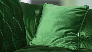close up of green velvet sofa with matching square cushion resting on the arm