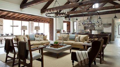 open plan living kitchen with dark beams and pale stone floors and camel colored sofas