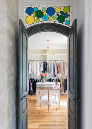 view through doors into work in wardrobe with stained glass above door, wooden floor, vanity and chair