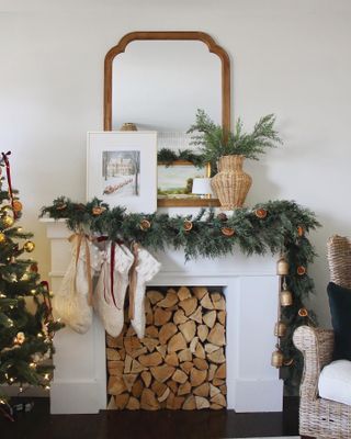 Evergreen garland with dried oranges over a white mantel filled with firewood