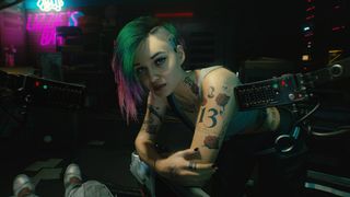 Judy in Cyberpunk 2077, one of V's romance options, bending down and looking at V in a chair.