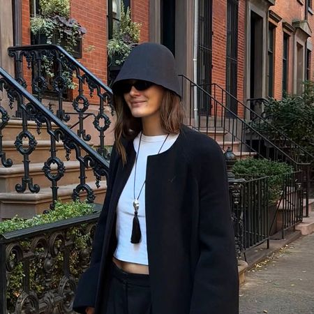 a woman wearing a bucket hat with a white t-shirt, black coat, and black sunglasses
