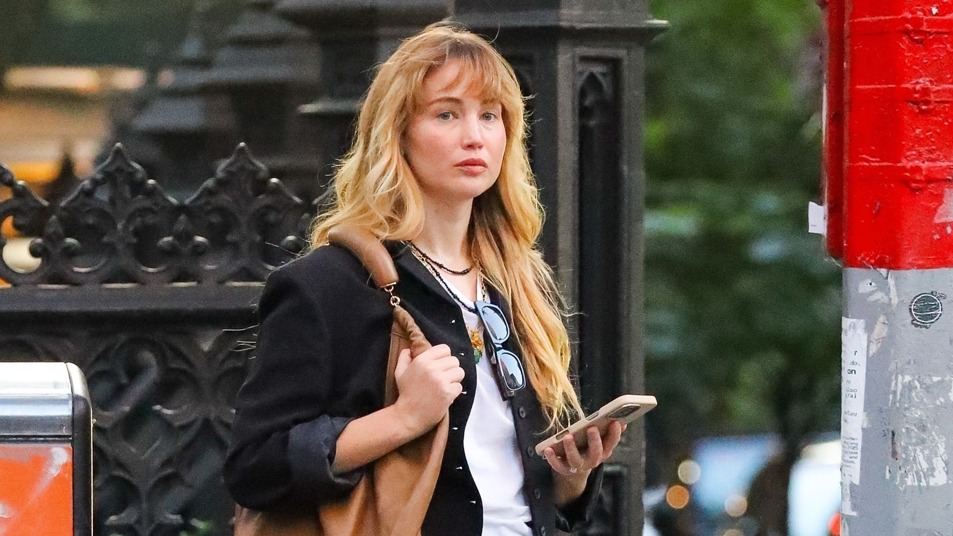 Jennifer Lawrence wearing a black button-up, white T-shirt, black skirt, black flats, and brown leather bag