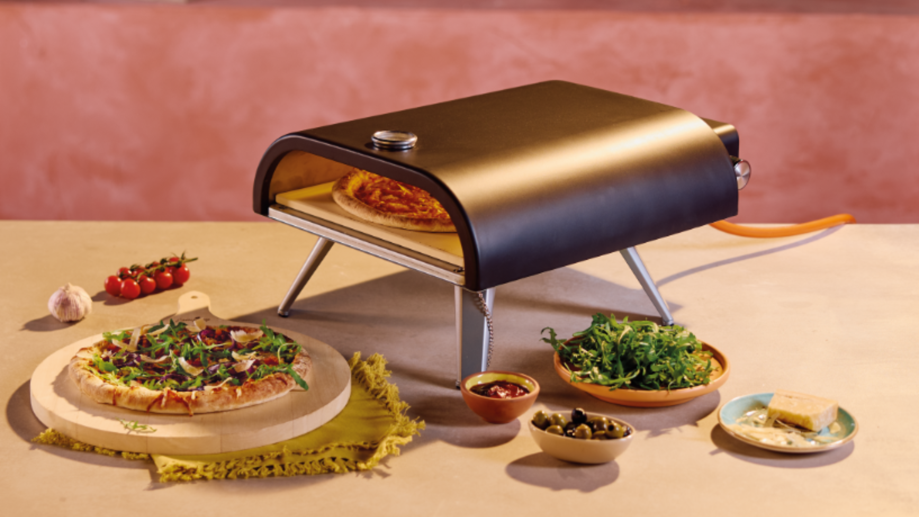 Aldi gas pizza oven on an outdoor kitchen worktop, with a cooked pizza and side dishes next to it.