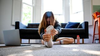 Woman with leg out in front of her, stretching and following at-home tutorial