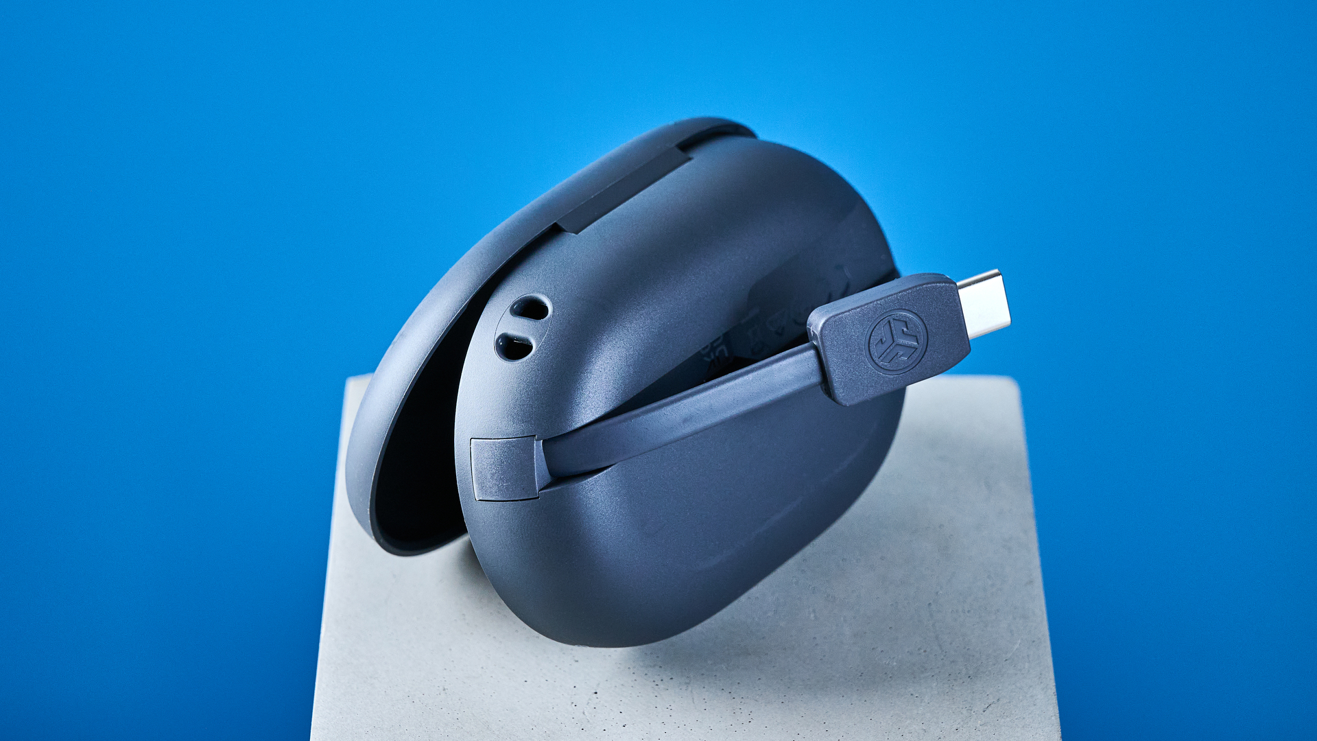 the jlab go sport+ earbuds photographed against the blue tom's guide background, showing charging case and wearing style