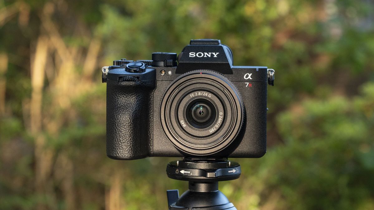 The Sony A7R VI camera with 24mm f/2.8 lens attached, it's mounted to a tripod outdoors, there's a natural background