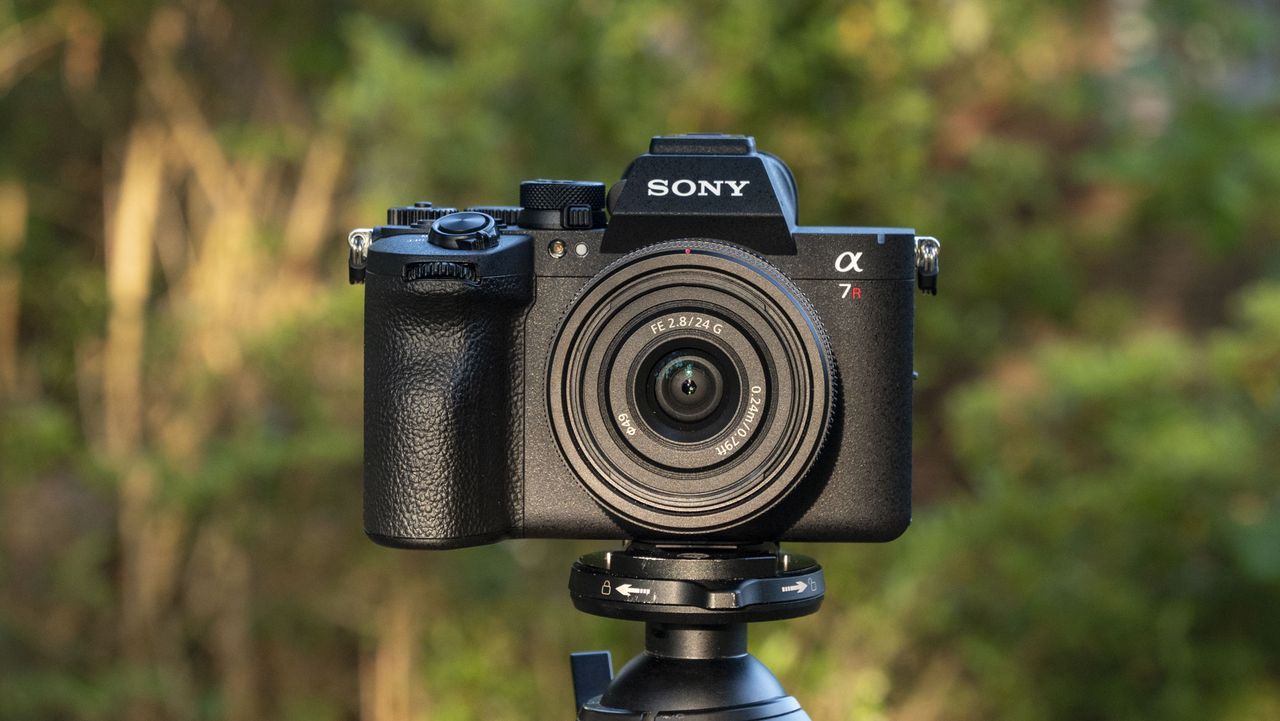 The Sony A7R VI camera with 24mm f/2.8 lens attached, it's mounted to a tripod outdoors, there's a natural background