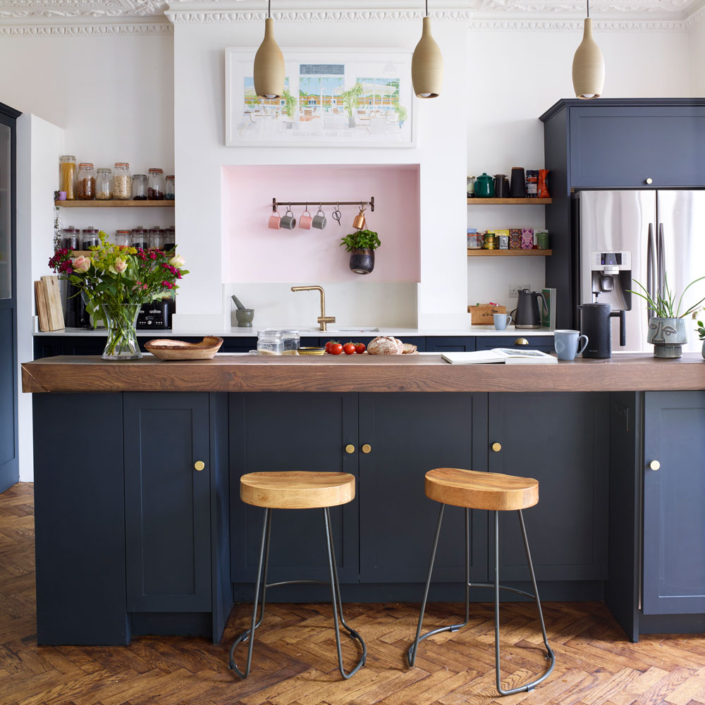 navy kitchen with wooden herringbone flooring, artwork and an island