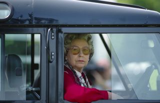 Queen Elizabeth wearing a red top and sticking her arm out the window of her Land Rover