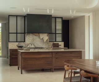 A dark wood kitchen with marble countertops and backsplash and glass fronted wall cabinets