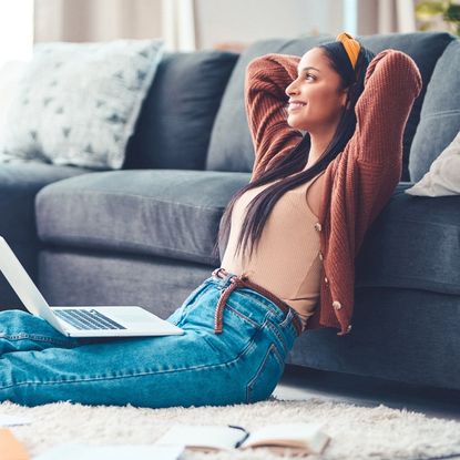 Shot of a young woman relaxing in the living room at home with her laptop and planning books open.
