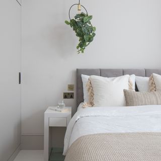 White walled bedroom with neutural white and grey bed and hanging plant