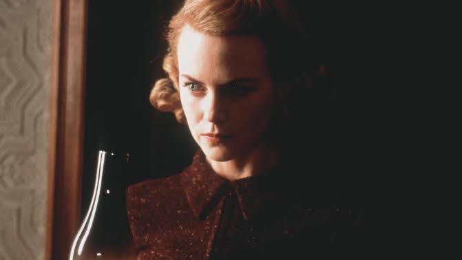 Nicol Kidman standing in the shadows holding an old fashioned oil lamp in a still from The Others.