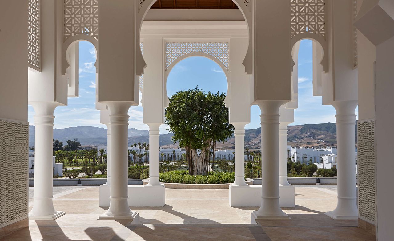 Exterior of the Banyan Tree Tamouda Bay hotel with large white stone archway and green shrubs and trees