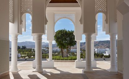 Exterior of the Banyan Tree Tamouda Bay hotel with large white stone archway and green shrubs and trees