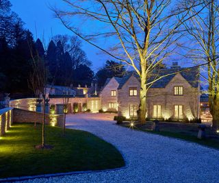 A gravel driveway leading up to a collection of brick houses with spotlights leading the way