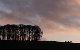 Three riders going up a hill against a cloudy background