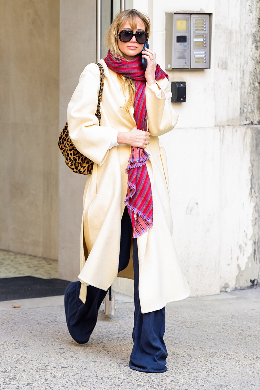 Jennifer Lawrence wearing a pale yellow coat, colorful scarf, La Ligne pants, Nike sneakers, and Dior sunglasses.