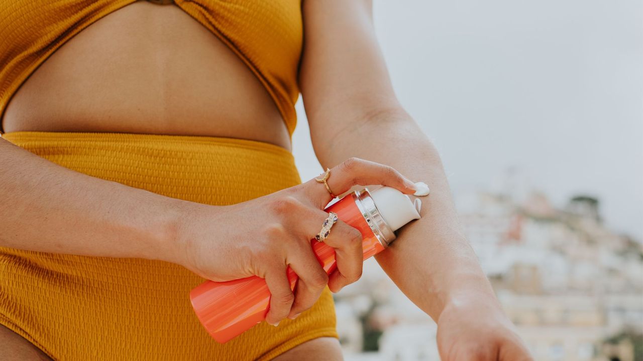 Woman in an orange bikini applying sun cream to her arm while at the beach