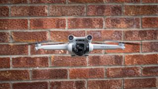 Dronen DJI Mini 3 Pro i flukt foran en murvegg.