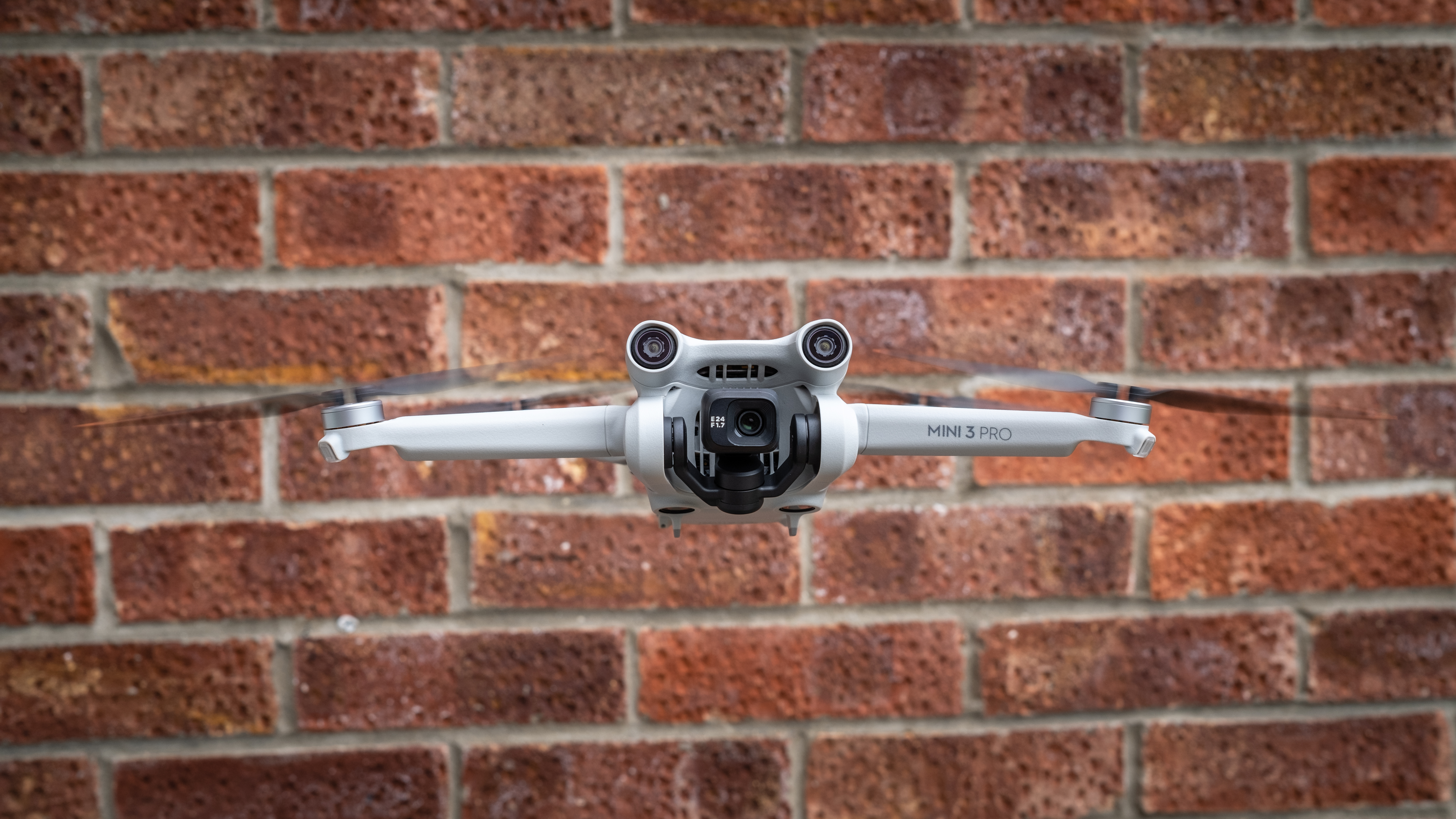 The DJI Mini 3 Pro drone, one of the best beginner drones, in flight in front of a brick wall