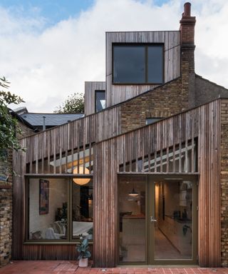 A three storey house extension with pale timber cladding with pitched roof