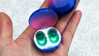Someone’s hand holding a pair of the Loop Engage earplugs in their case in a jewelled turquoise shade.