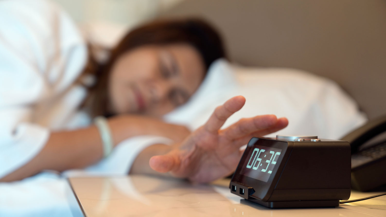 A person reaching for the snooze button on their alarm clock