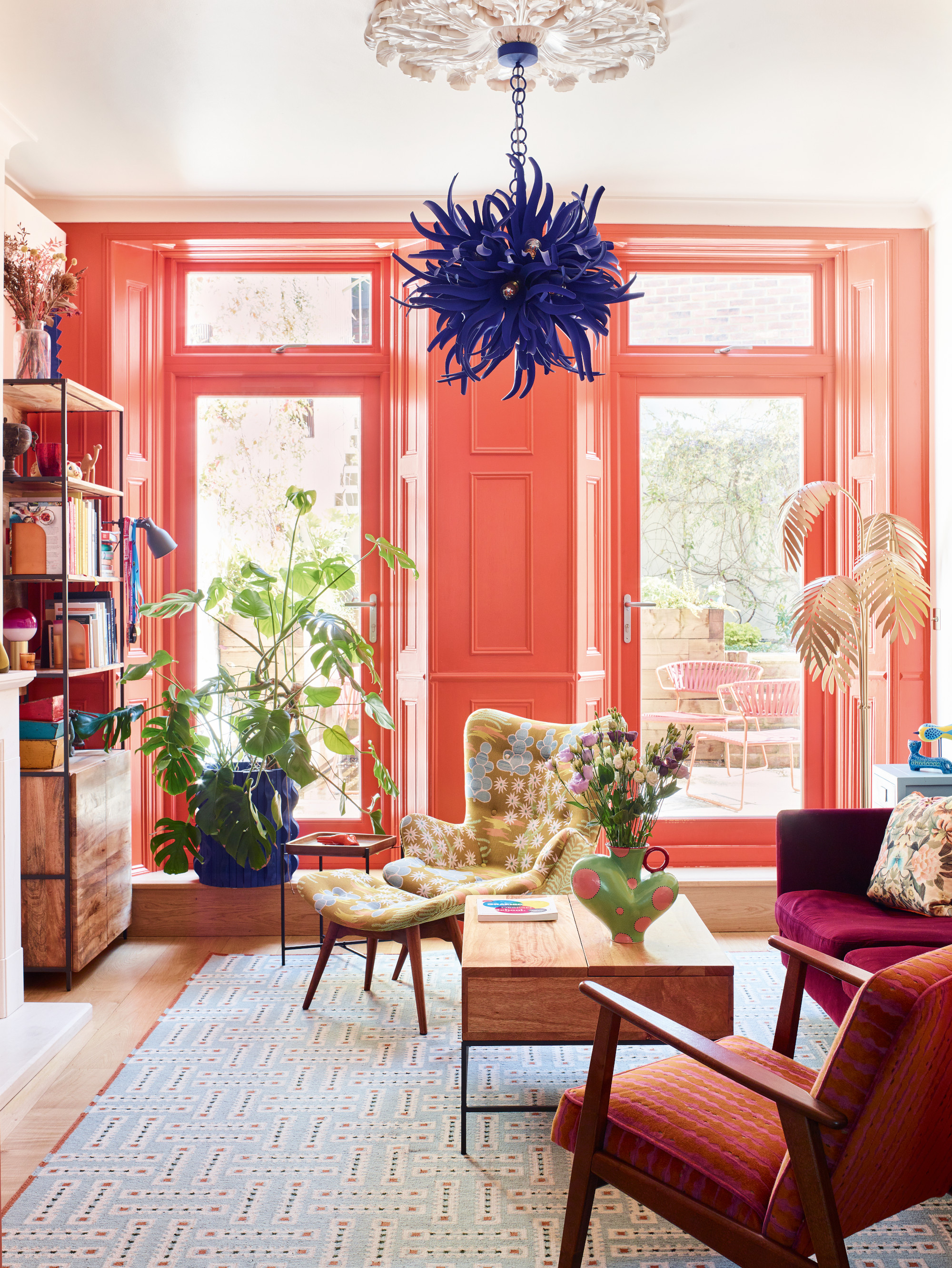 Coral living area with pink, terracotta and lime green seating, industrial wood coffee table and shelving, cobalt blue pendant light and blue and red patterned rug