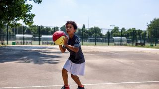 African boy plays basketball outdoors on sunny day.