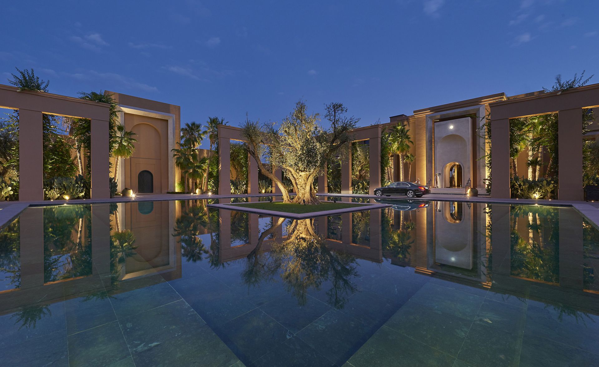 A large hotel pool with an island with a tree in the middle surrounded by palm trees and stone columns.