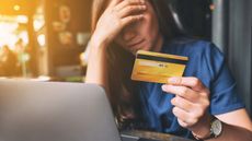 Stressed young woman holds credit card and looks at laptop