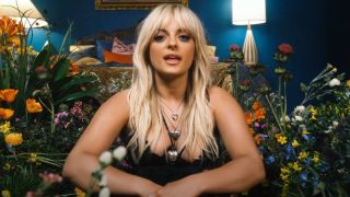 Bebe Rexha talking to the camera from the flower set of her music video Sabotage.