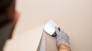 A person sliding a putty knife under a section of tan-colored wallpaper