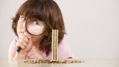 A young girl checks out a stack of gold coins using a magnifying glass.