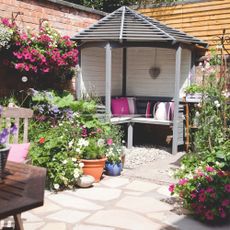 Corner of a patio with lots of plants in pots and a corner pergola seating area