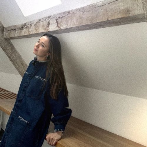 Image of a woman in a denim dress leaning on a wooden countertop in a white room.