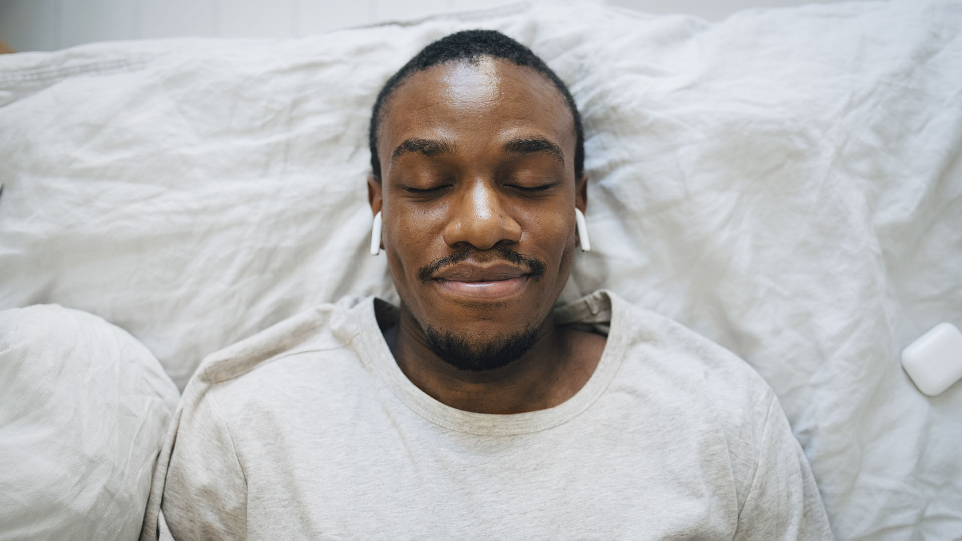 Man lying in bed with eyes closed and Airpods in
