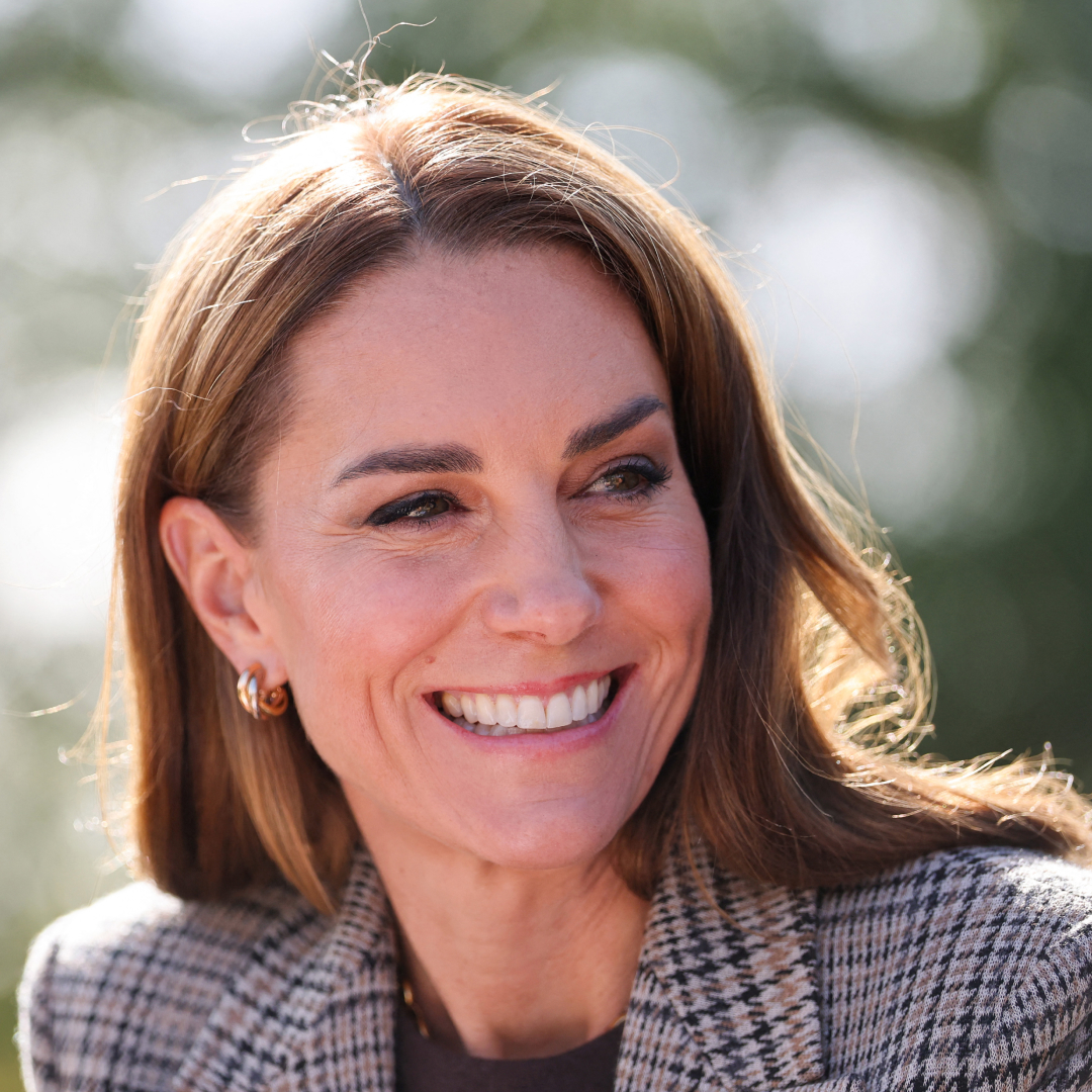 Princess Kate wearing a plaid blazer and smiling in front of a tree