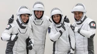 four astronauts in white spacesuits giving thumbs up to camera
