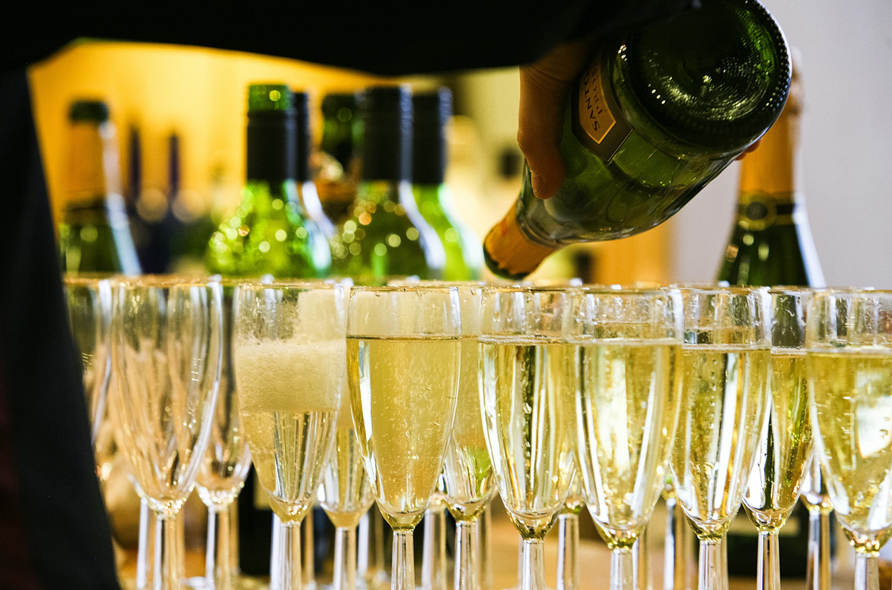 A person pouring from a bottle of sparkling wine into glasses on a bar top best cava under &pound;25